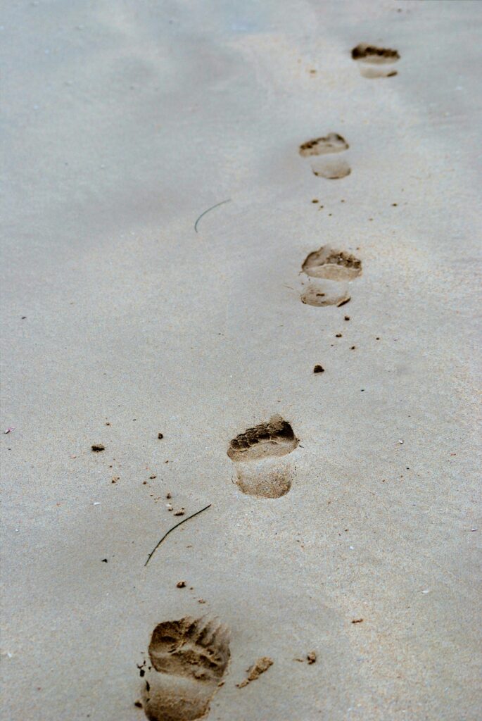 Deep footprints in beach sand, symbolizing the structural and fascial patterns that develop in the body.