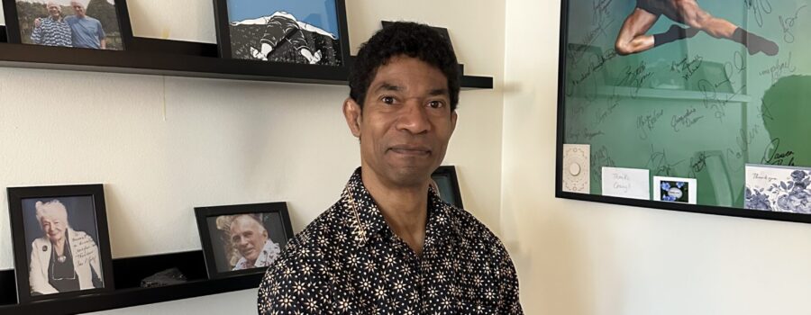 Craig Dunham, Rolf Method of Structural Integration practitioner in Los Angeles, seated in his Santa Monica office with photos of Dr. Ida Rolf and his teachers — Emmett Hutchins, and Neal Powers — behind him.