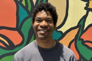 Craig Dunham, Advanced Rolf Method practitioner, standing in front of a colorful mural outside his Santa Monica office building.